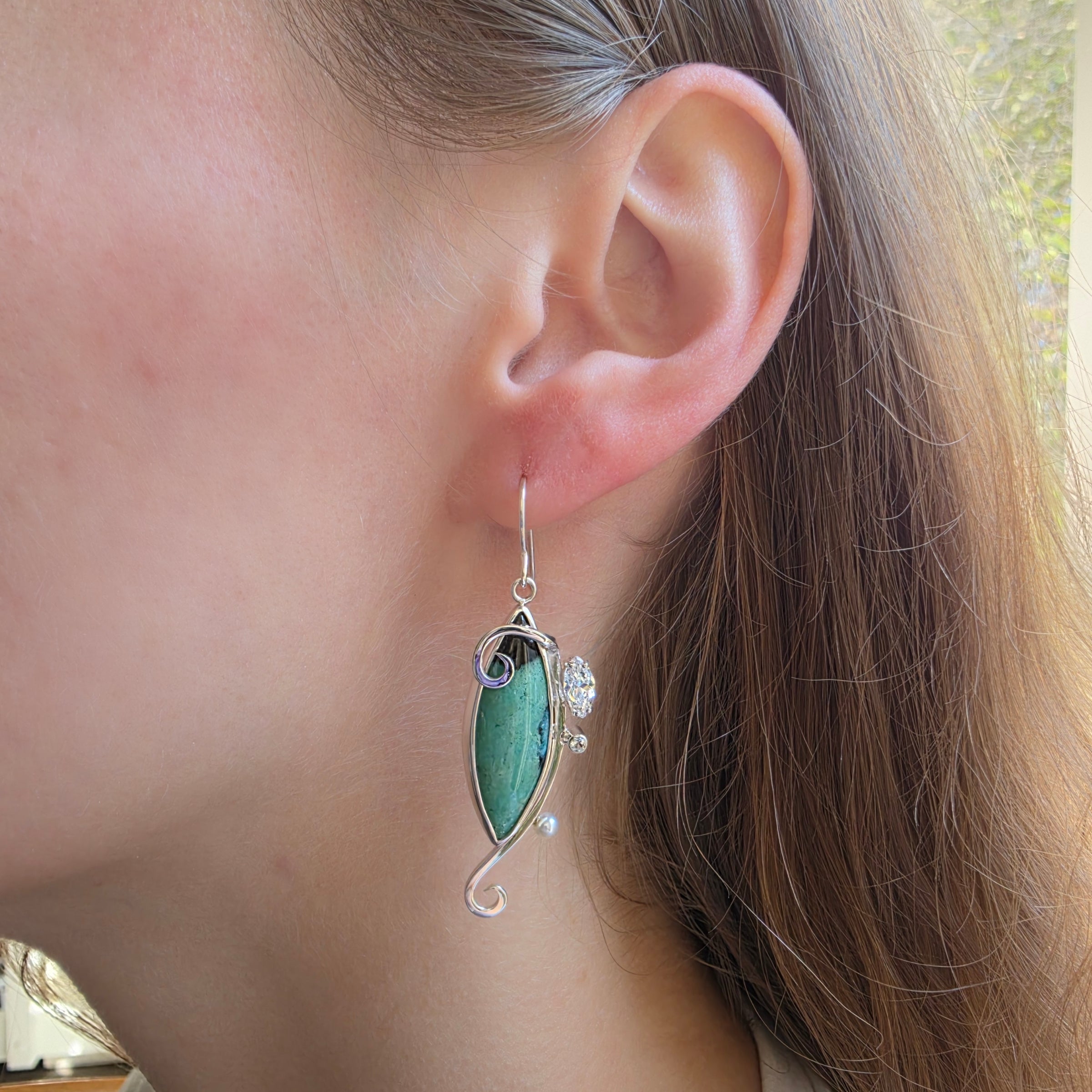 Modeling picture of Asymmetric Opalized Wood earrings with Swiss Blue Topaz, Peridot and Freshwater Pearls set in Sterling Silver.