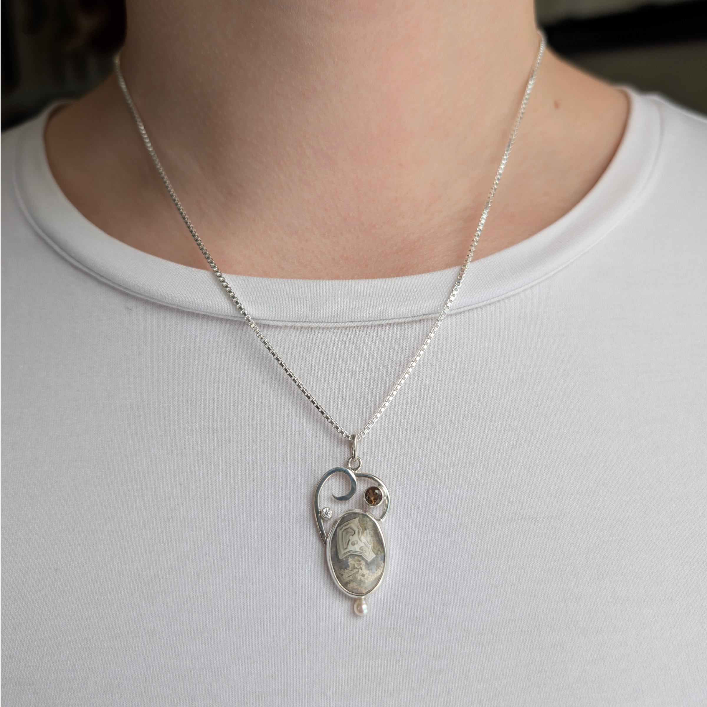 Sterling Silver pendant with Crazy Lace Agate, Smokey Quartz, Cubic Zirconia and Freshwater Pearl, includes an 18 inch Sterling Silver chain on a model.