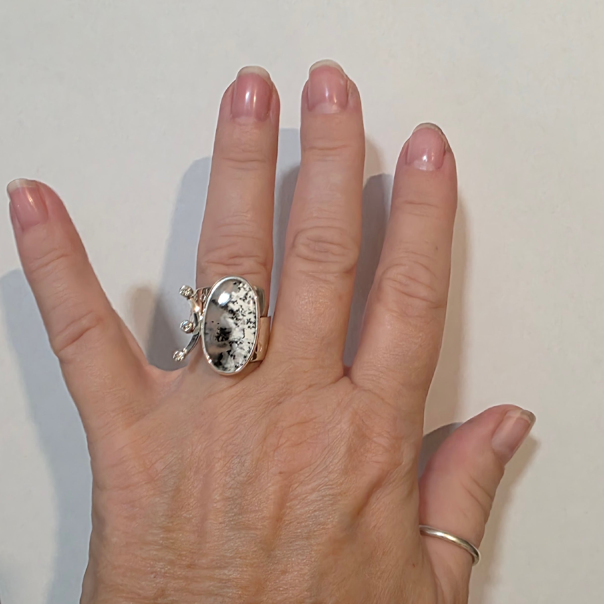 Adjustable Sterling ring with black and white Dendritic Opal and Cubic Zirconia on a model's hand.